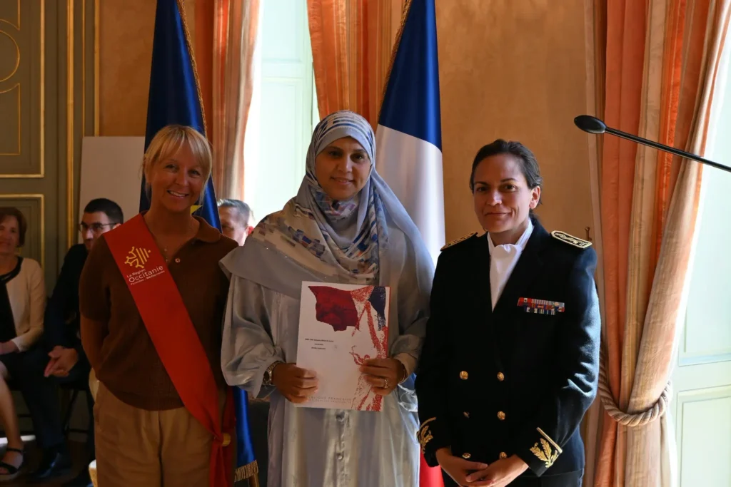 Photo de cérémonie de naturalisation : une participante tenant un dossier avec des représentantes des autorités
