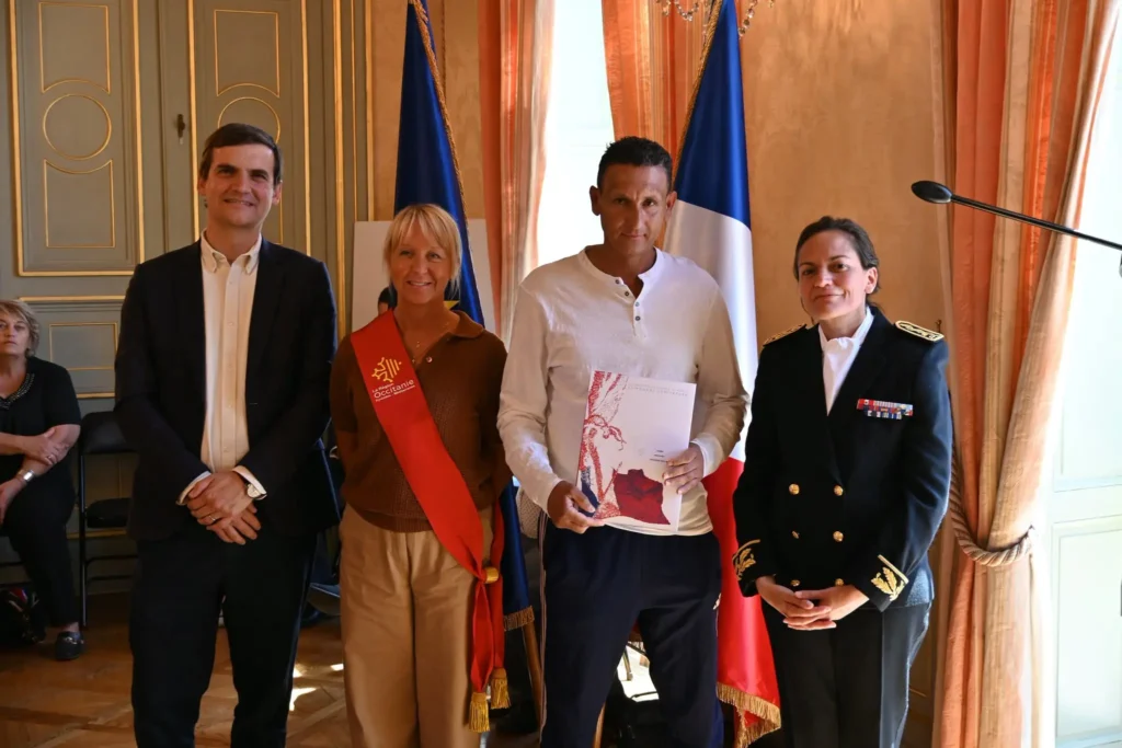 Photo de cérémonie de naturalisation : un participant entouré de représentants officiels devant les drapeaux